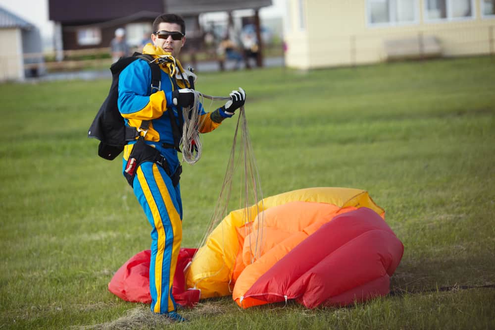 Male skydiver holding his parachute slings after landing. Standing on green lawn.