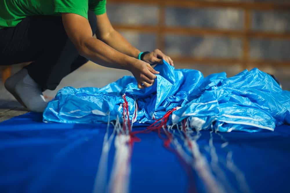 Male skydiver packing a light blue parachute before jumping.
