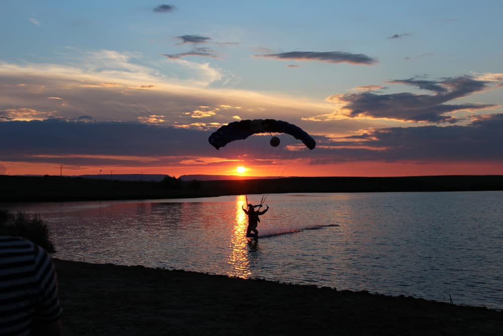 Skydiver swooping into a pond / lake in the sunset.