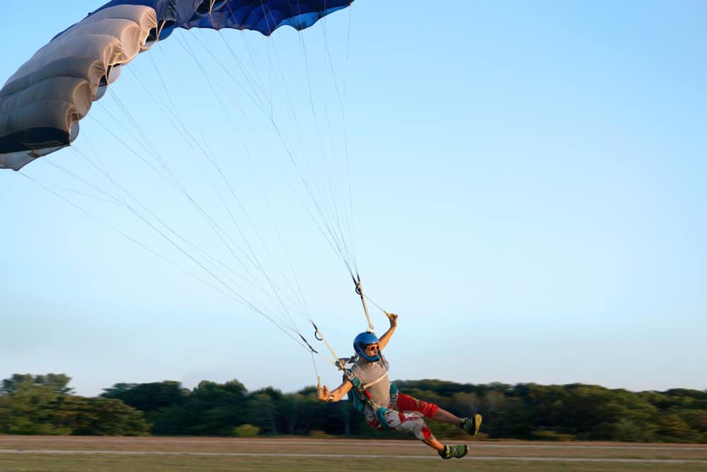 Skydiver under a dark blue little canopy of a parachute is landing on airfield.