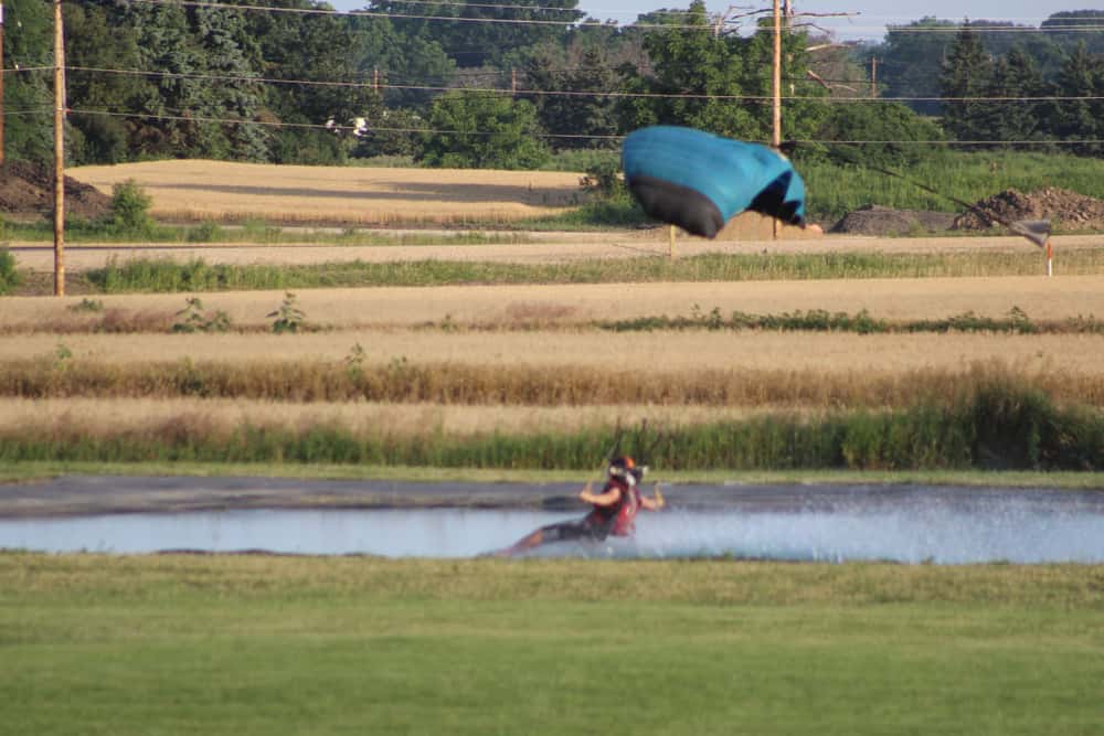 Skydiver swooping into a small lake surrounded by corn fields.